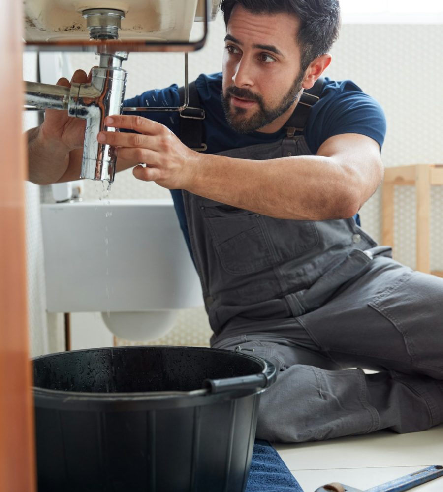 Male Plumber Working To Fix Leaking Sink In Home Bathroom